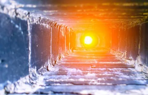 A warm light flows through a narrow tunnel made of bricks, illuminating the i Stock Photos