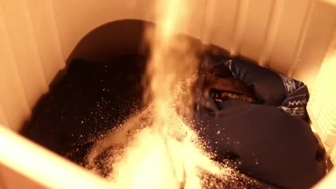 Warm Light on Laundry as Detergent Powder Pours into Washing Machine Stock Footage 339069313