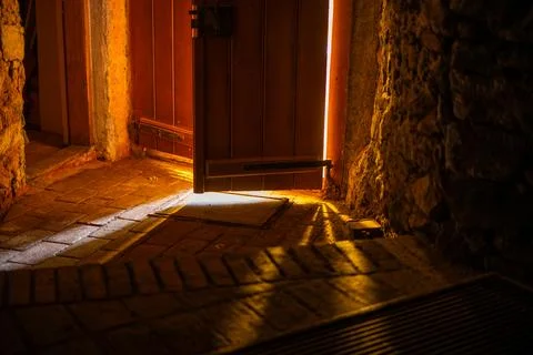Warm Light Streaming Through a Partially Open Wooden Door in a Rustic Stone.. Stock Photos