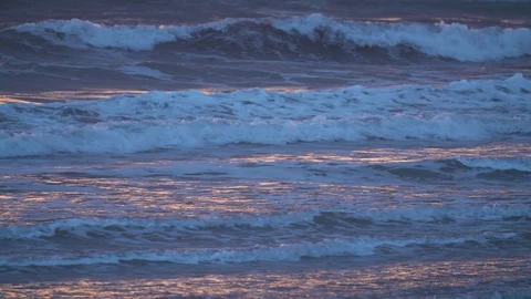 The warm light of the sunset reflecting in waves on a beach Stock Footage 124998072