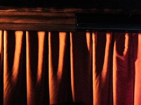 Warm light through dark stage curtains Stock Photos