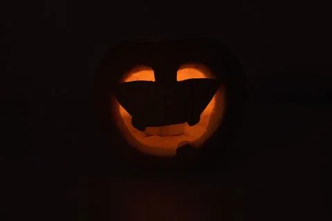 Warm lit jack o lantern face creates spooky halloween decor with carved eye.. Stock Photos