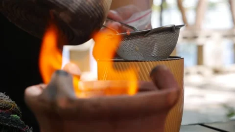 Warm milk tea flows through a sieve into a ceramic cup, blending heritage and Stock Footage 312337021
