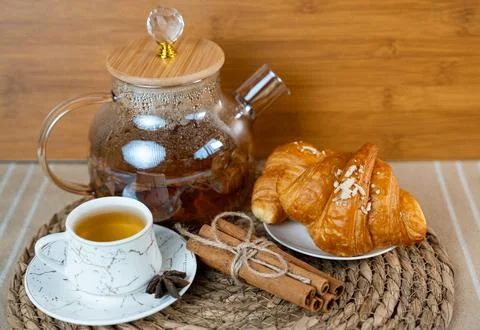 Warm morning table with cup of tea, glass teapot, and croissants. Cozy homemade Stock Photos
