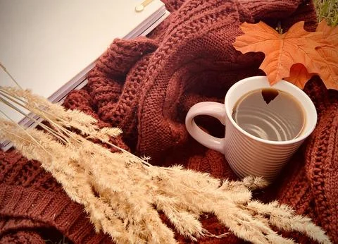 A warm mug of coffee rests inside a knitted sweater, surrounded by dried grass Foto stock