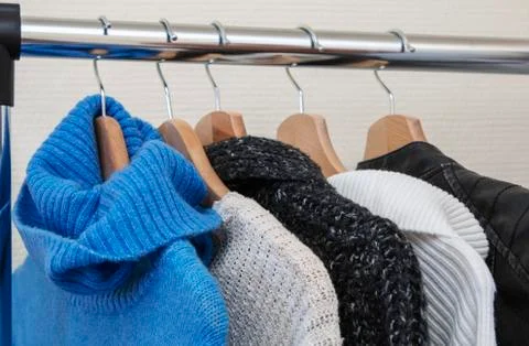 Warm multi-colored knitted sweaters hang on wooden trempels Stock Photos