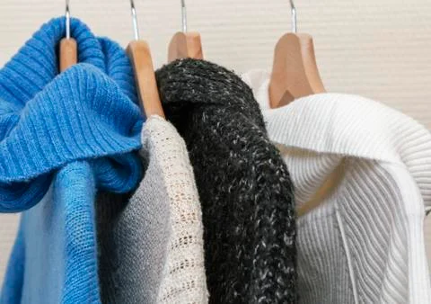 Warm multi-colored knitted sweaters hang on wooden trempels Stock Photos