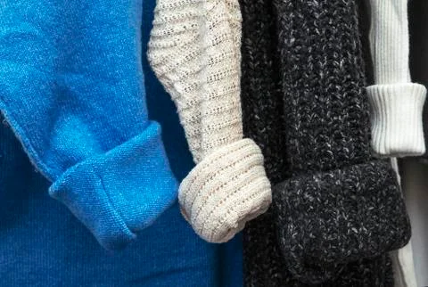 Warm multi-colored knitted sweaters hang on wooden trempels Stock Photos
