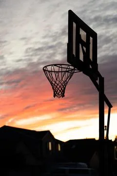 A warm multi colored reds and purples sunset behind a basketball hoop Stock Photos