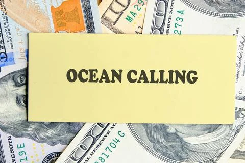 A warm note with the words Ocean Calling rests atop scattered dollar bills, s Stock Photos