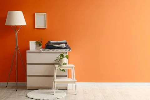 Warm plaids on commode and floor lamp near orange wall Stock Photos