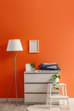 Warm plaids on commode and floor lamp near orange wall Stock Photos