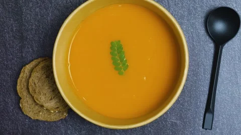 Warm pumpkin soup nestled in ceramic bowl, green herb garnish, crusty bread Video stock 314887722
