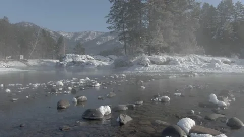 A warm rocky river surrounded by pine forest and mountains in winter Stock Footage