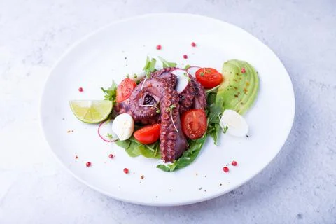 Warm salad with octopus, cherry tomatoes, avocado, arugula, quail eggs. Stock Photos
