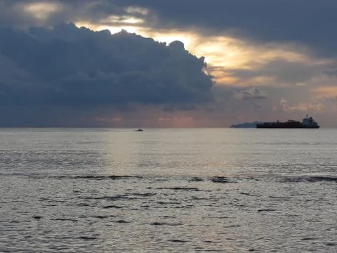 Warm sea sunset with cargo ship and a small fishing boat at the horizon Stock Photos
