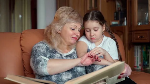 Warm slow motion shot senior woman shows little girl family album Stock Footage 152829692