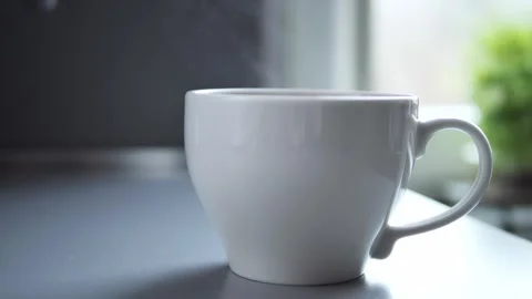 Warm steam curling from white ceramic mug, soft window backdrop featuring Stock Footage 302840191
