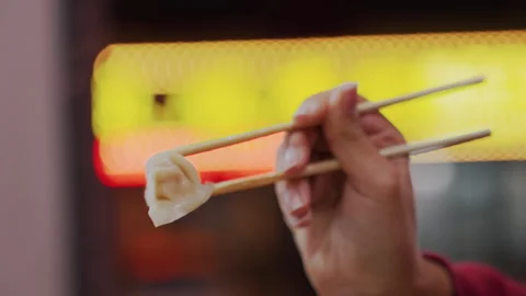 Warm steamed dumpling grasped with chopsticks in city alley. Nighttime urban Stock Footage 337318041
