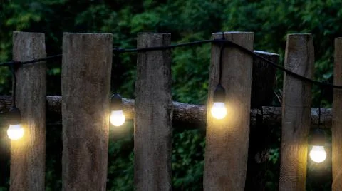Warm string lights draped over a classic wooden fence, evoking a cozy and n.. Stock Photos
