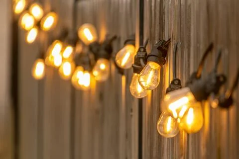 Warm string lights glow softly against a wooden wall, creating a cozy and inv Stock Photos