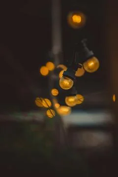Warm string lights hanging outdoors create a cozy, inviting vibe against a .. Stock Photos