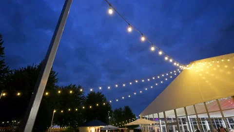 Warm string lights illuminate an outdoor venue under a dramatic blue evening Stock Footage 340448884