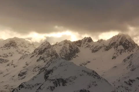 Warm sun rays breake through winter clouds. Alps mountains. Stock Photos