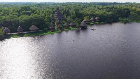 Warm sunlight glinting across river surface, eco friendly wooden houses lining Stock Footage 308420345