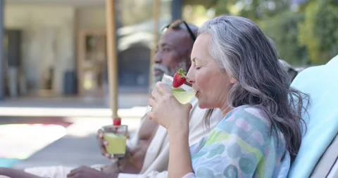 Warm sunlight urging mature couple lounging poolside sipping mint cocktails with Stock Footage 342721100