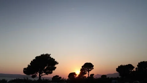 Warm sunset behind pine silhouettes overlooking the calm sea and distant mountai Stock Footage 341556850
