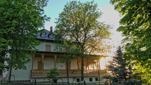 Warm sunset light passing by a building, trees, and a wrought iron fence Stock Footage 334840564