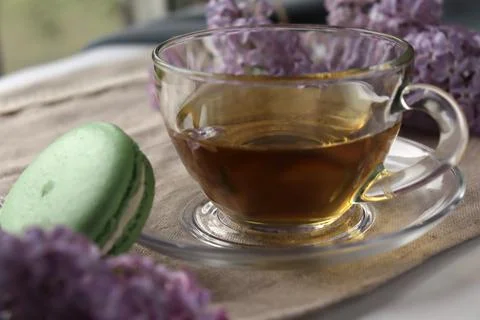 Warm tea in clear cup with macaroon and lilac flowers on a table during Stock Photos