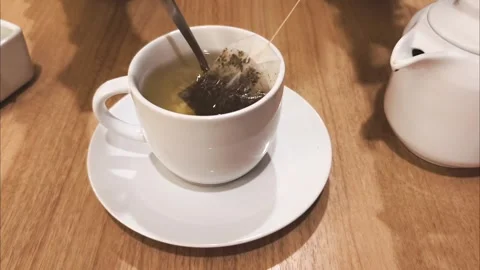 Warm tea steeping in a white ceramic cup. Soft light glows over wooden table. Stock Footage 339744308