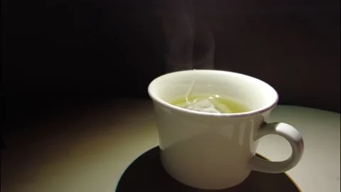 Warm white tea cup with a tea bag, smooth smoke water steam black background Stock Footage 149842658