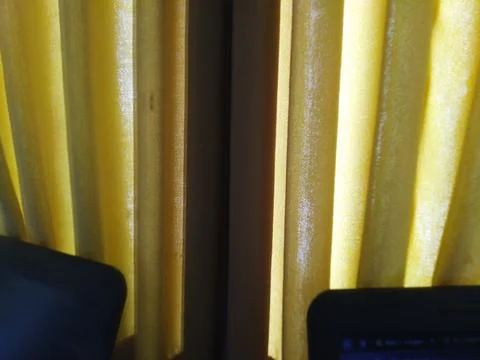 Warm yellow curtains create a soft background with laptop devices visible bel Stock Photos