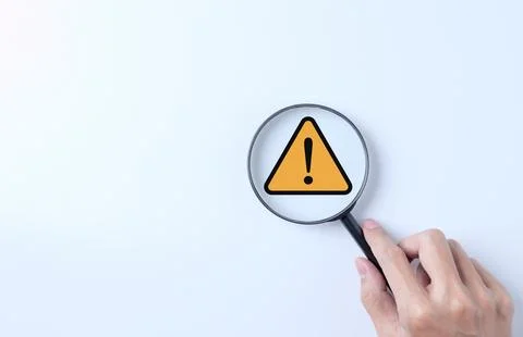 Warning alert system concept. Magnifying glass focused on yellow triangle. Stock Photos
