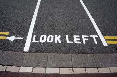Warning message "look left" on footpath crossing street Stock Photos