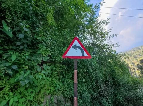 Warning Road Sign Indicating Sharp Left Turn on a Narrow Mountain Pass Stock Photos