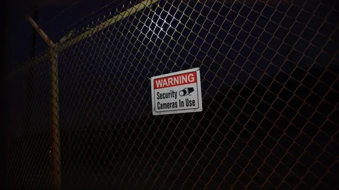 Warning Security Cameras In Use sign on a fence at night Stock Footage 126689062