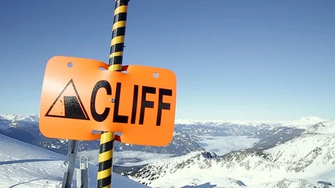 A warning sign on Blackcomb indicating a cliff is nearby with mountains in the Stock Footage 101779982