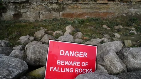 Warning sign of falling rocks below cliff at staithes uk Stock Footage 138808863