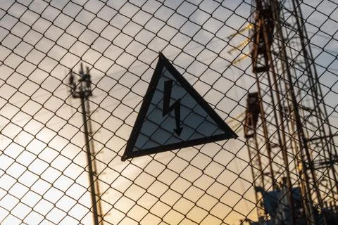 Warning triangular sign with a lightning image on the net fence. Dangerous - Stock Photos