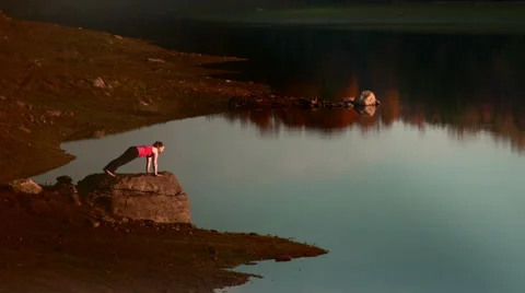 Warrior II yoga pose variations on rock near lake Stock Footage 44119976