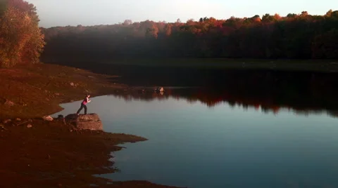 Warrior III to extended leg pose on rock near lake Stock Footage 44119756
