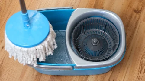 Washing and spinning the flat mop telescopic handle in a blue bucket filled with Stock Footage 122381475