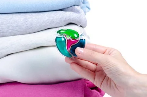 Washing capsules in hand, stack folded clean washed laundry Stock Photos