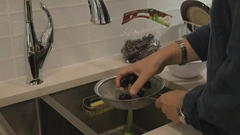 Washing cherries in a strainer above kitchen sink. Видео 101365702
