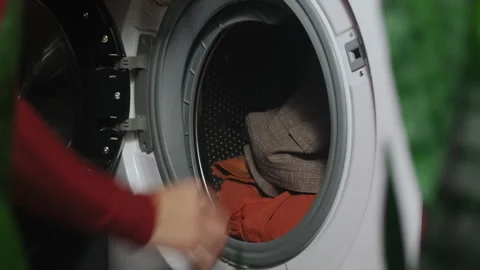 Washing clothes. Hands load dirty laundry into washing machine. Stock Footage 253604403