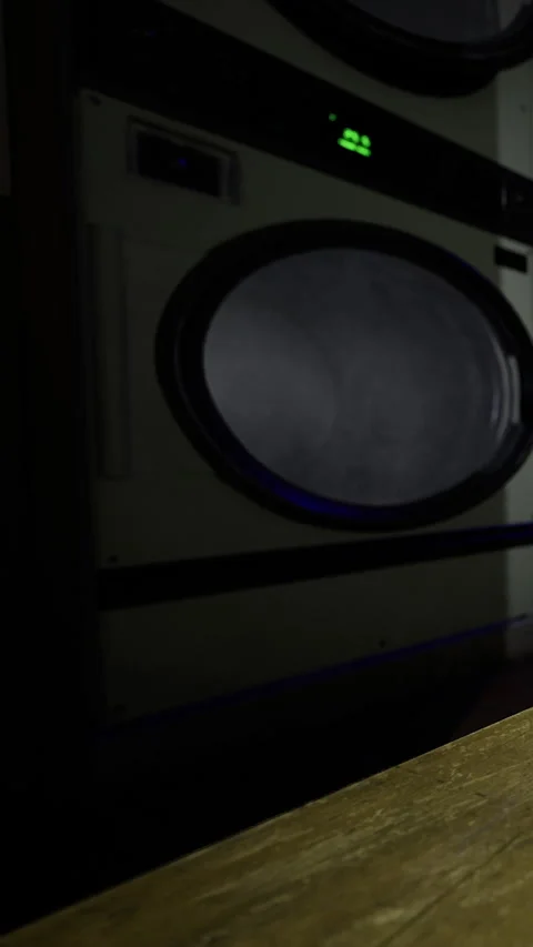 Washing clothes in a laundromat at night with empty machines in view Stock Footage 331688284